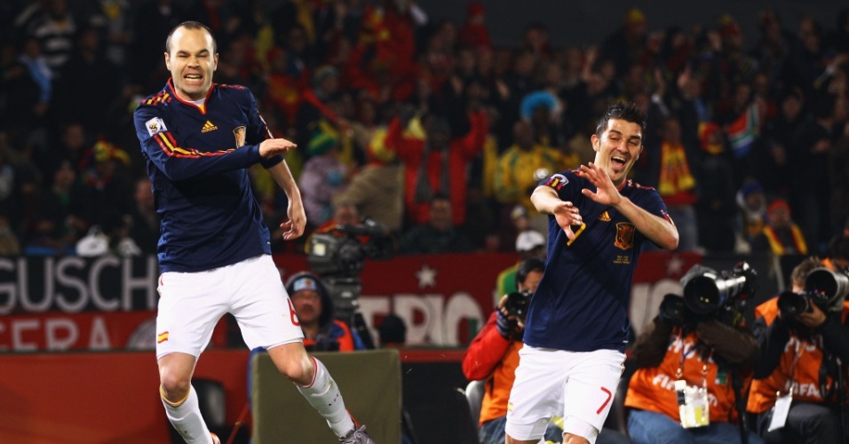 Iniesta dá uma tapa na bandeira de escanteio e David Villa se protege após gol da Espanha