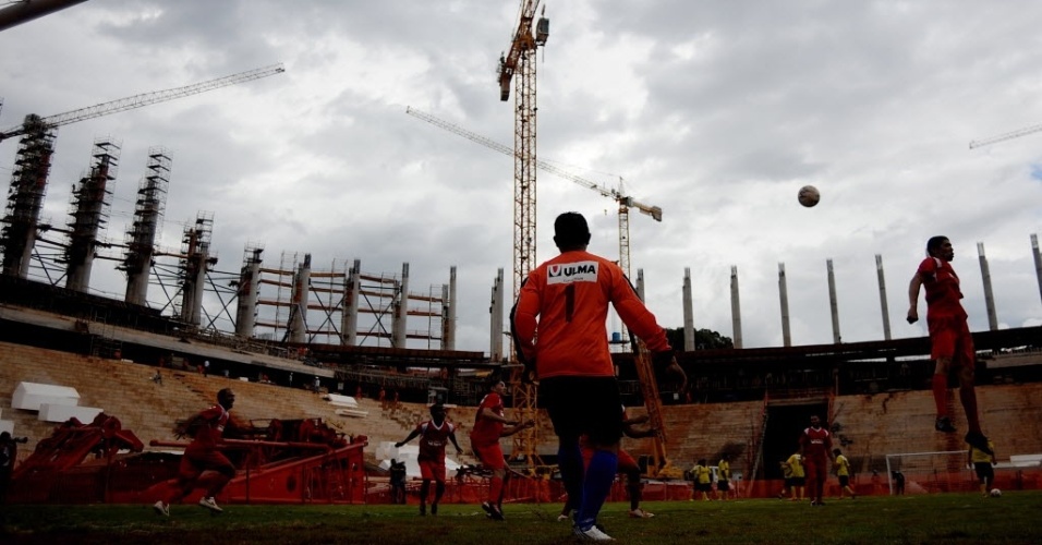 Operário das obras no Estádio Mané Garrincha, em Brasília, tenta cabeceio durante partida realizada no campo durante as reformas